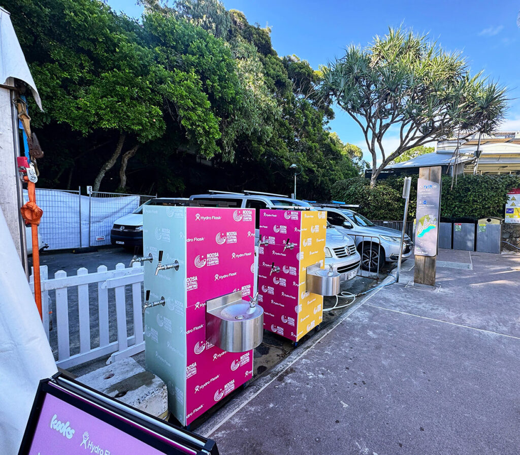 Colorful public water stations beside parked cars.