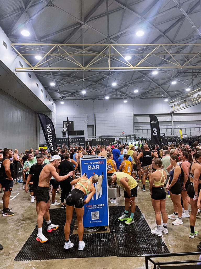 Crowd using water station at indoor fitness event.