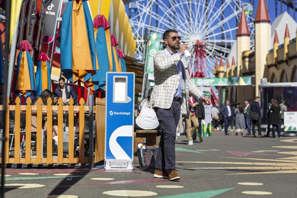 Man drinking near colorful umbrellas and amusement park.